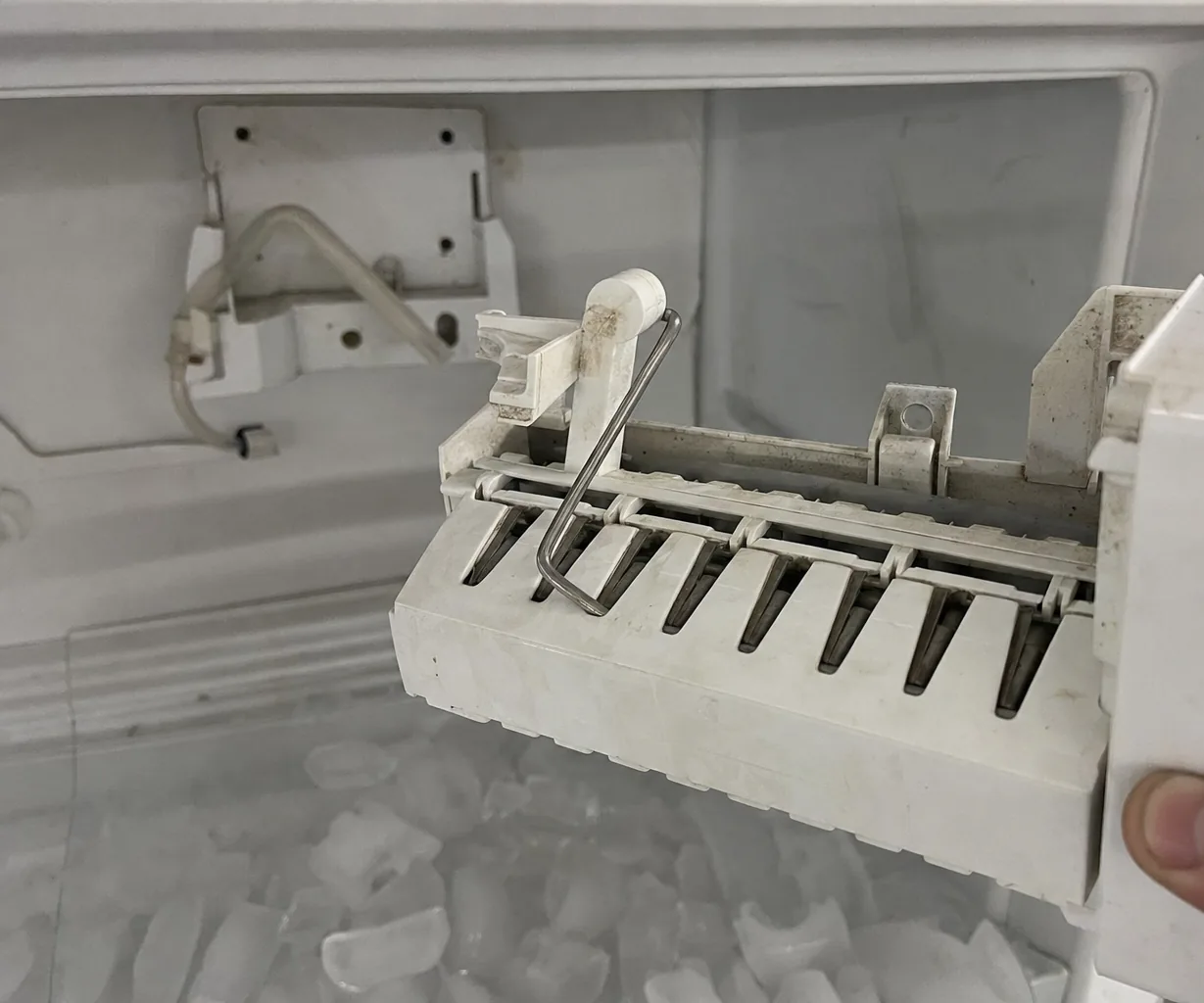 Mirrored right-hand crop of the ice maker module in hand, the empty bracket and fill tube stub sharp behind it.
