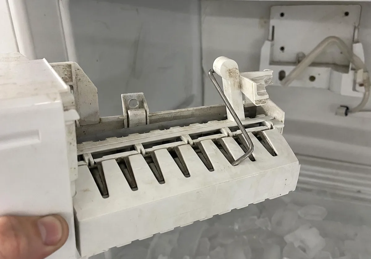 Centre crop of the lifted ice maker module, white plastic housing and harvest arm filling the frame.