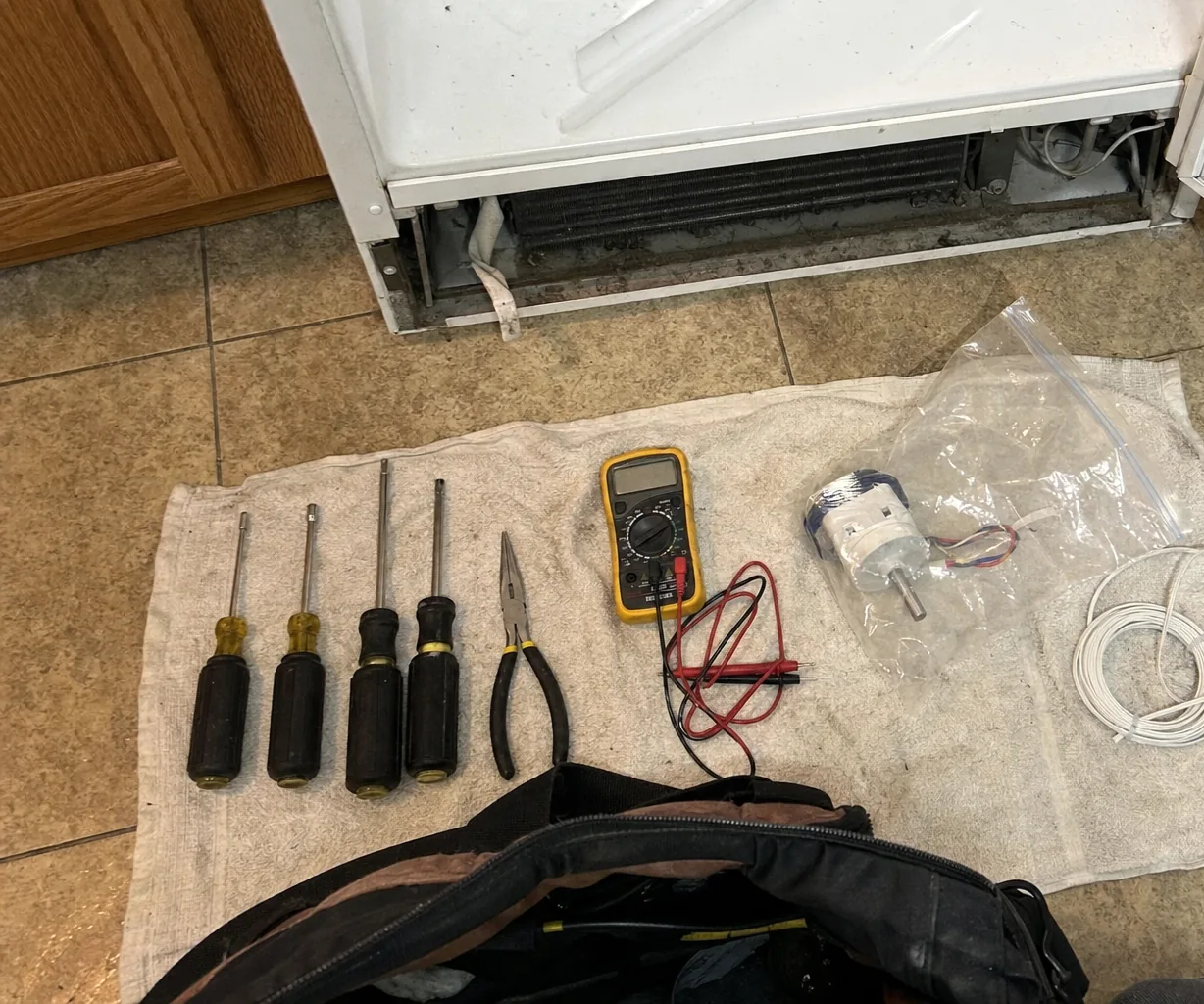 Left portion of the tool flat-lay: the multimeter with its leads coiled, nut drivers fanned out beside it on the towel.